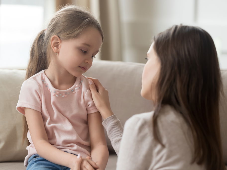 Kind sitzt auf dem Sofa und die Mutter spricht zu ihm