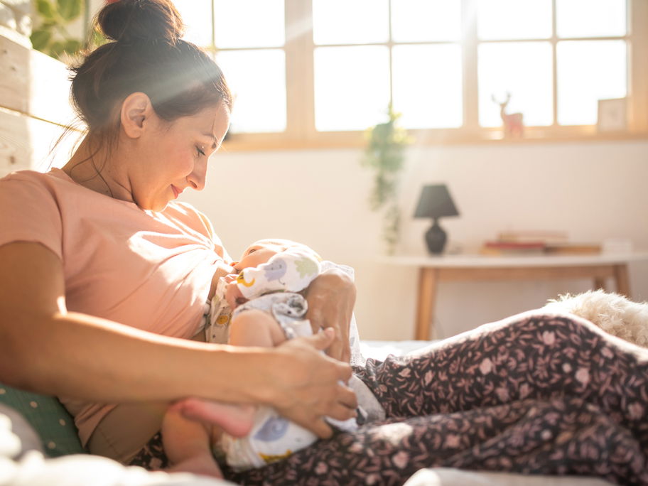 Dauernuckeln: Junge Mutter hält ihr Baby in den Armen zum Stillen und Nuckeln.