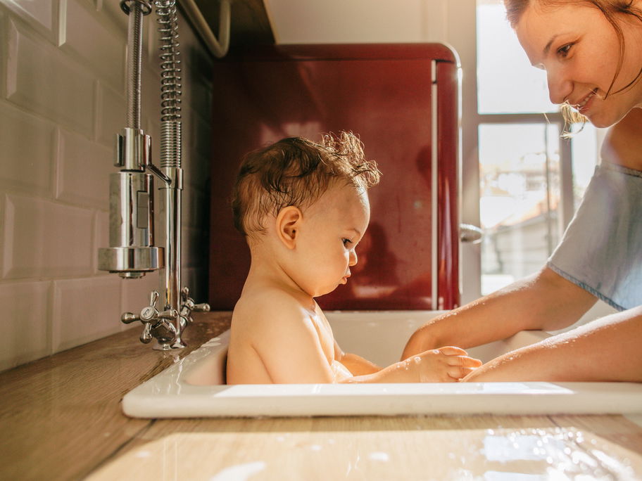 Eine junge Mutter badet ihr Baby im Waschbecken.