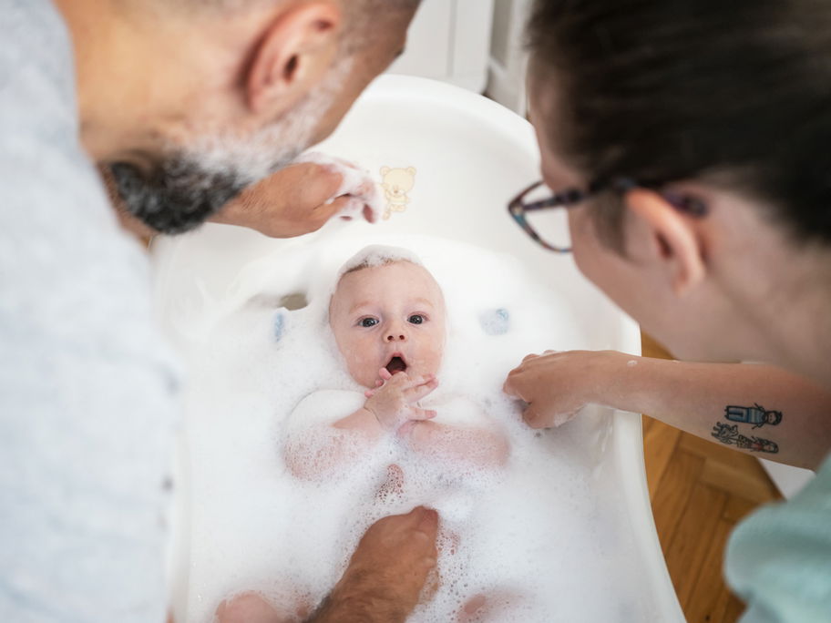 Eltern baden ihr Baby in einer Babybadewanne mit viel Badezusatz und Schaum.