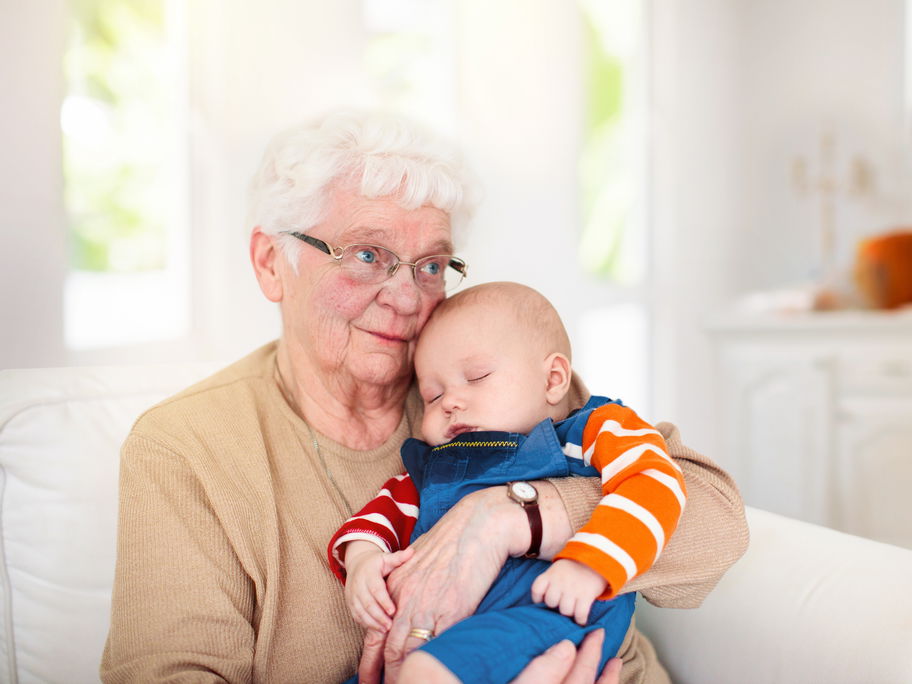 Oma hält schlafendes Baby im Arm.