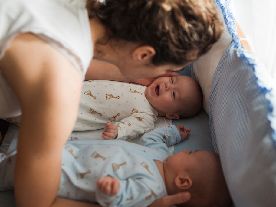 Mama legt zwei Babys ins Bett.