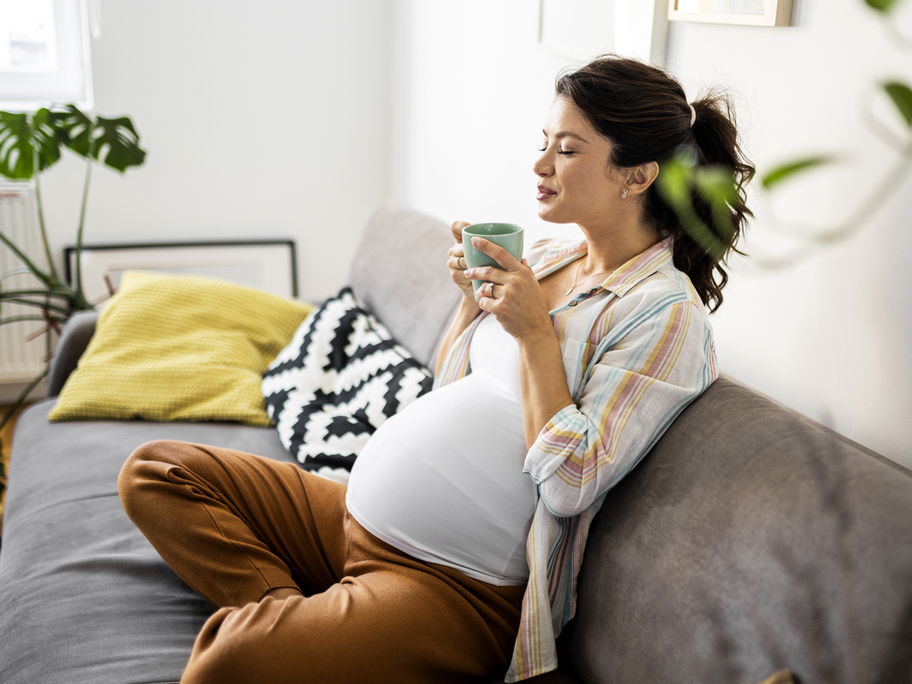 Eine Schwangere trinkt auf dem Sofa eine Tasse Tee.