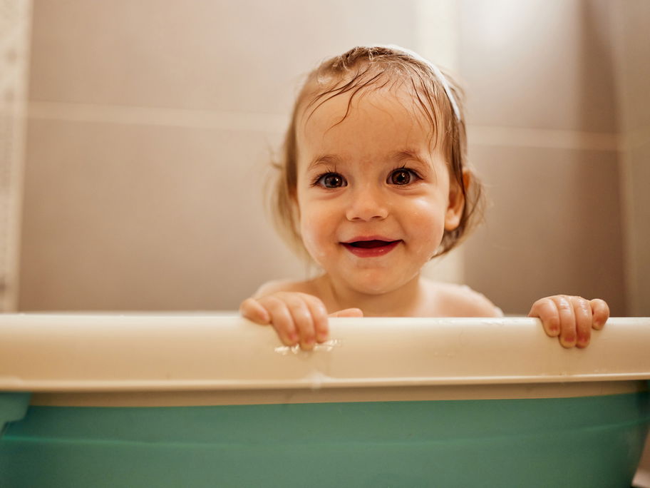 Baby-Mädchen schaut niedlich aus der Babywanne – aber wie lange?