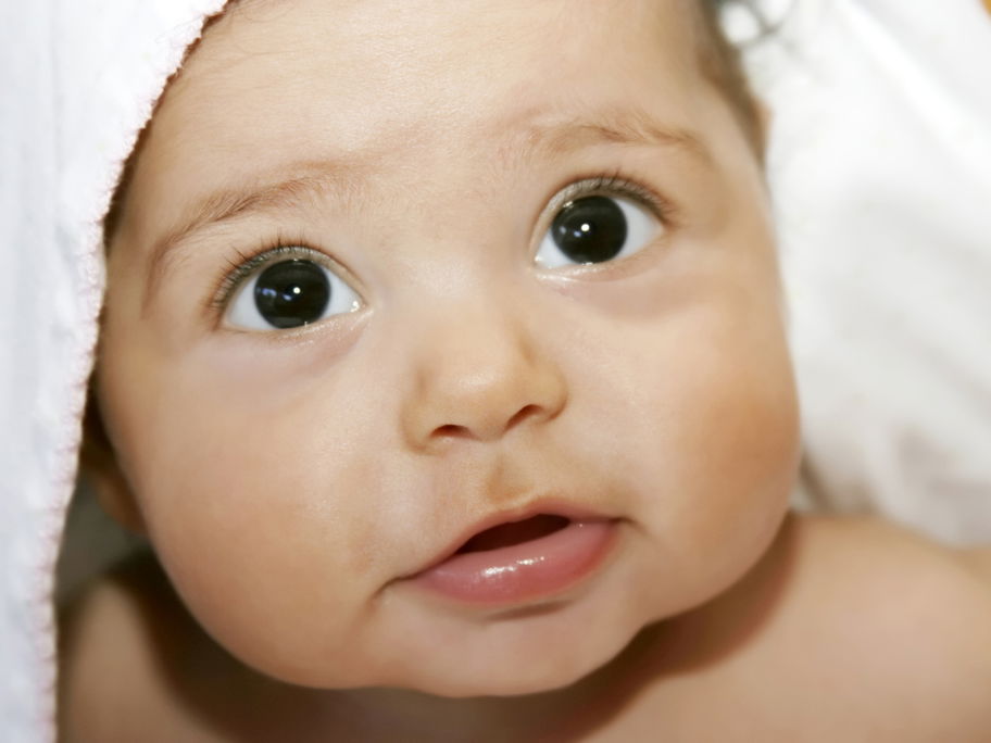 Niedliches Baby schaut eingewickelt in ein Handtuch mit Dackelblick in die Kamera.