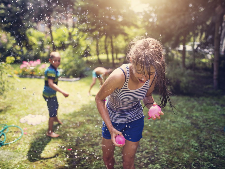 Zwei Kinder bewerfen sich im Garten mit Wasserbomben.