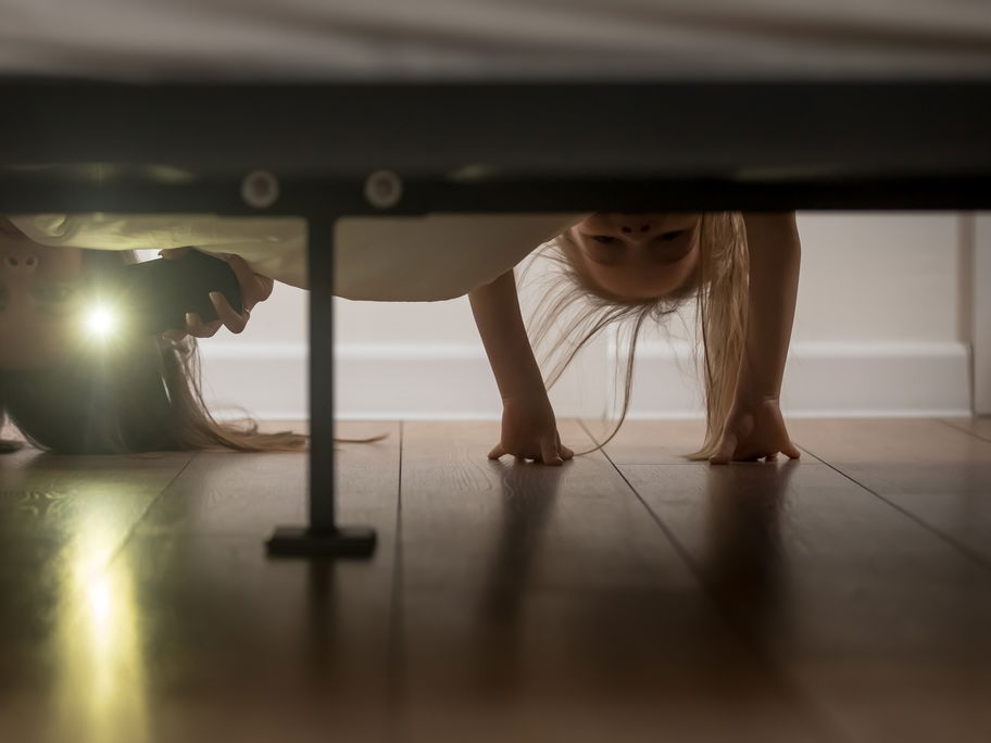 Mutter und Tochter schauen mit Taschenlampe unters Bett
