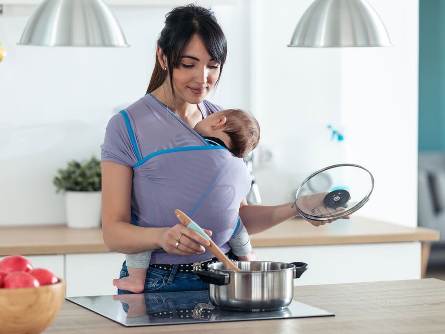 Mama mit Baby in Babytrage beim Kochen