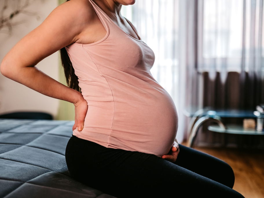 Hochschwangere Frau hält sich Bauch und Rücken
