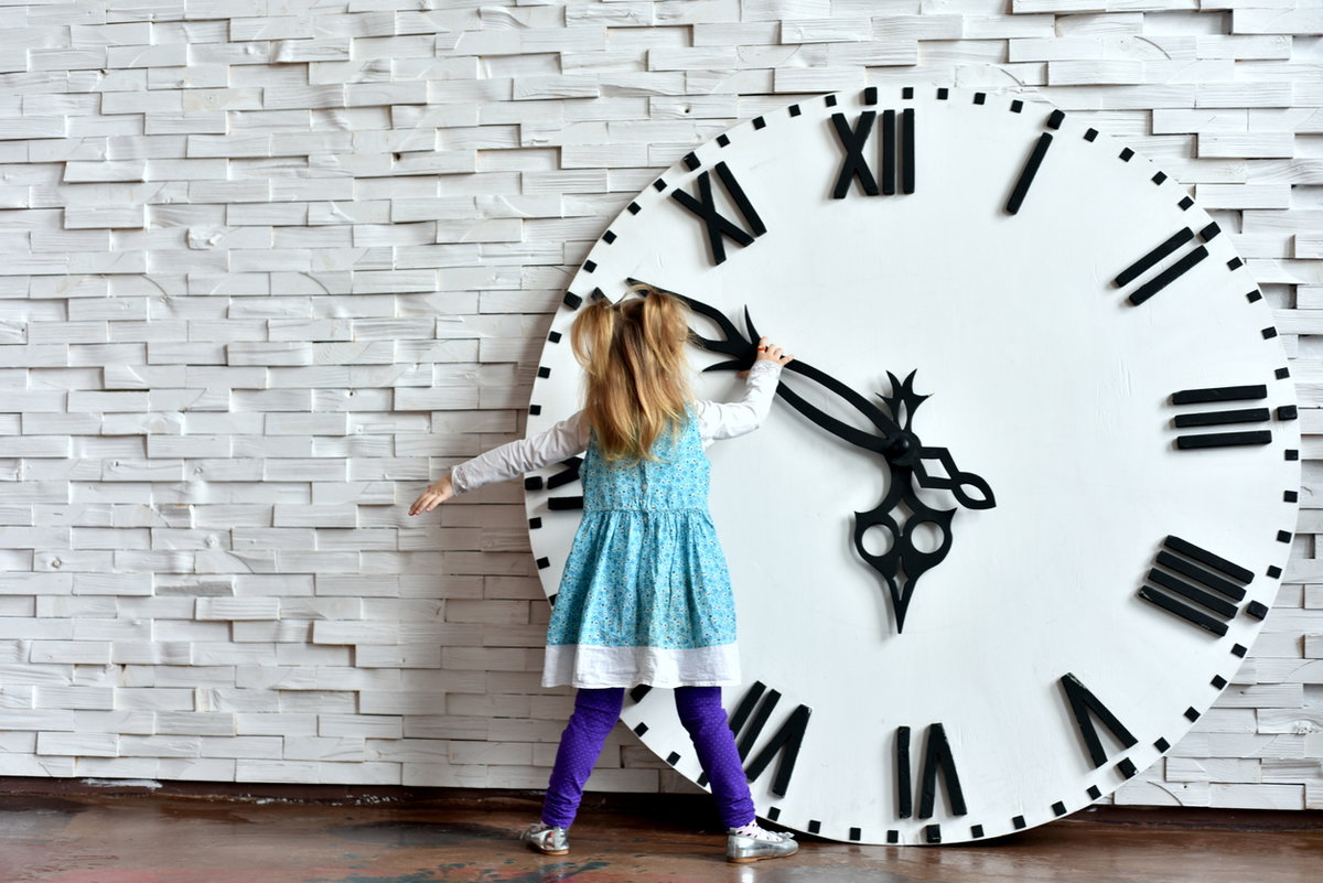 Kleines Mädchen steht vor riesiger Uhr