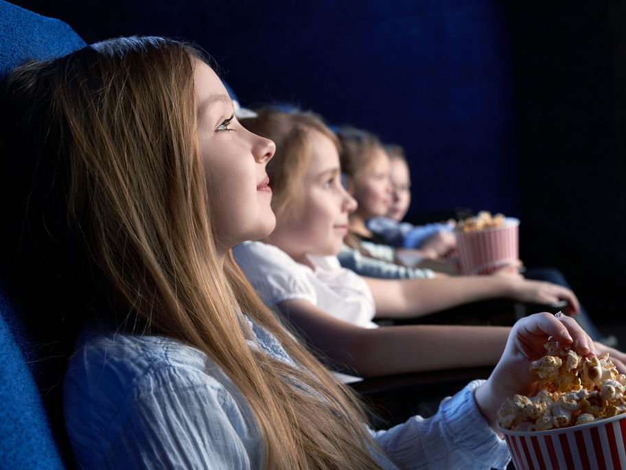 Junge Kinder sitzen im Kino und essen Popcorn.