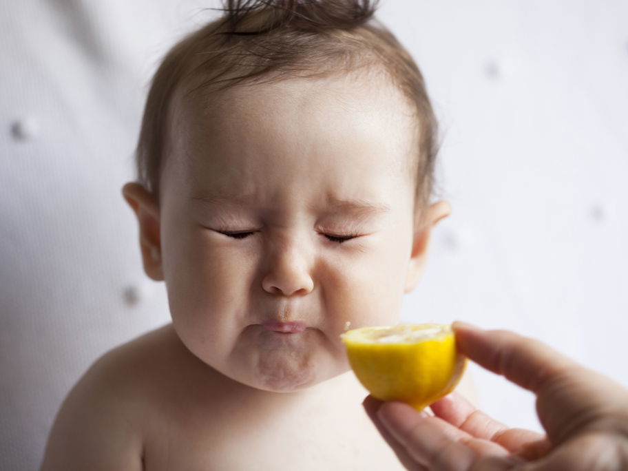 Ein kleines Baby isst eine Zitrone und verzieht das Gesicht.