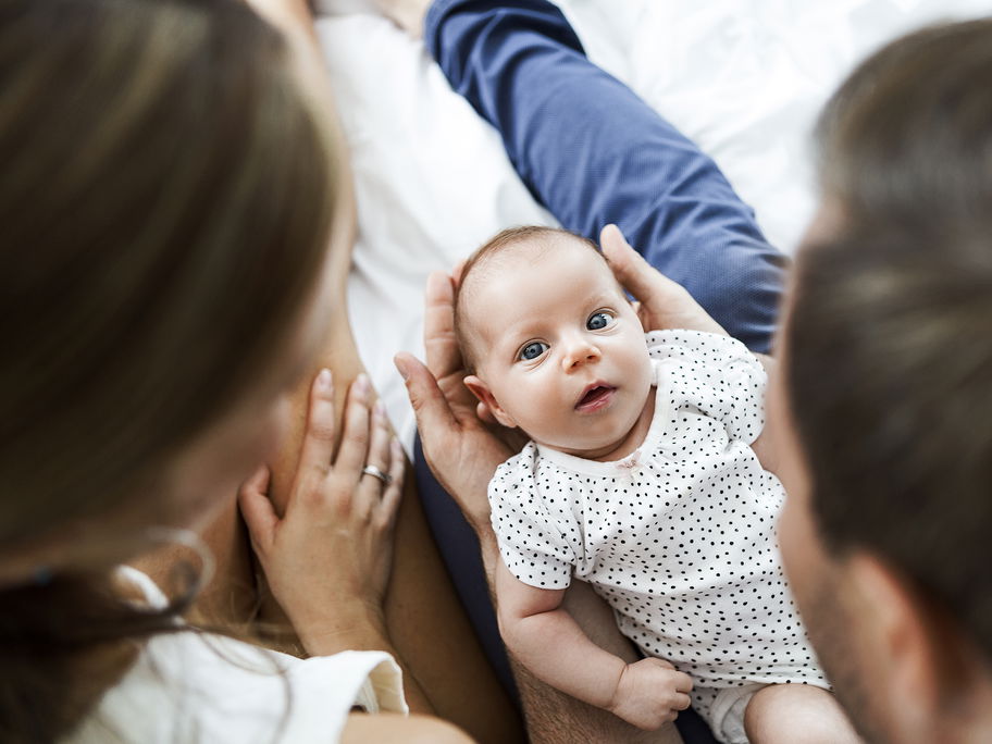 Mutter, Vater und Baby auf einem weißen Bett.