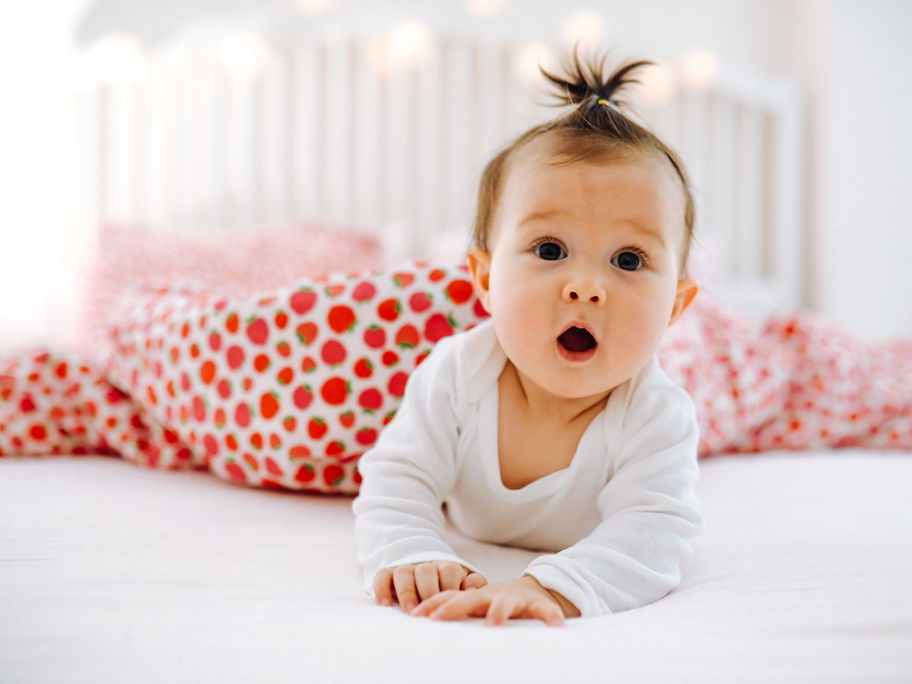 Baby mit erstauntem Gesichtsausdruck im Bett.
