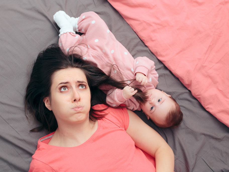 Mama liegt neben Baby auf dem Bett.
