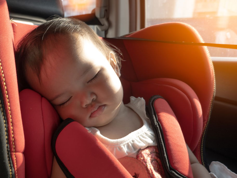 Ein Baby sitzt im Kindersitz des Autos, während die Sonne hereinscheint.