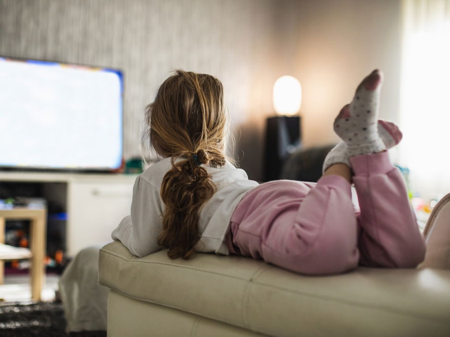 Ein Mädchen liegt auf dem Sofa und schaut eine Kinderserie.