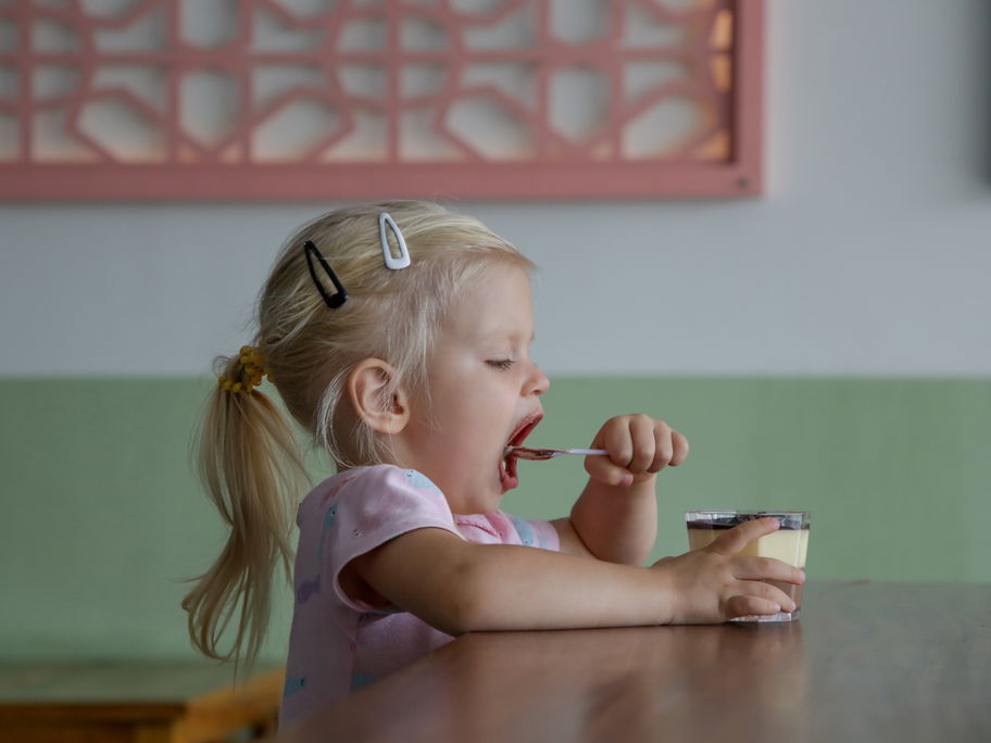 Kleines Mädchen löffelt Dessert.