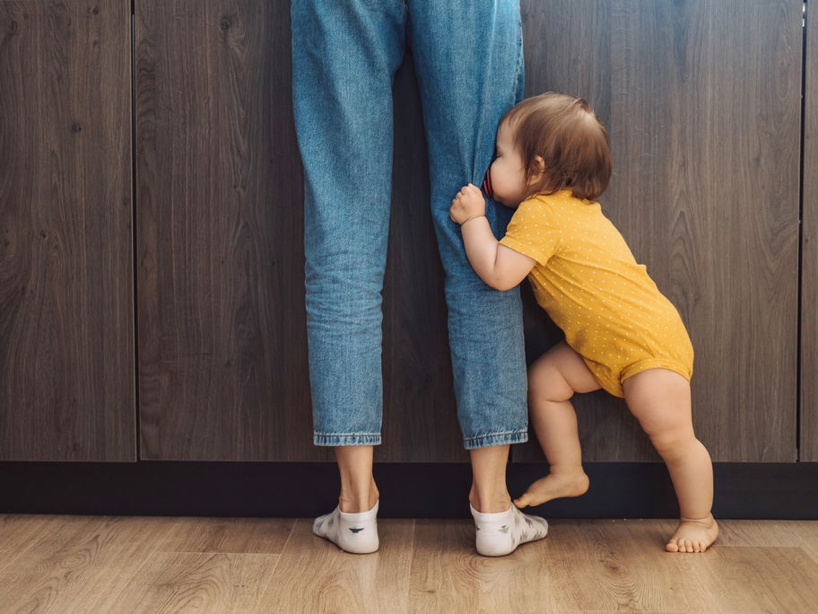Baby, das sein Gesicht hinter den Beinen seiner Mutter versteckt.