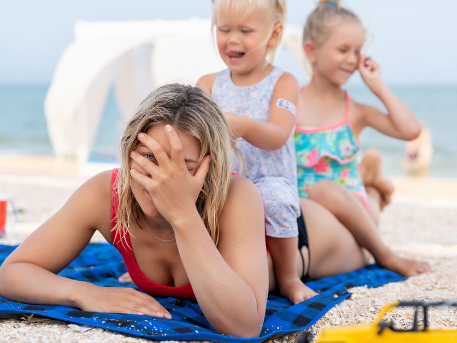 Zwei Mädchen sitzen am Strand auf dem Rücken ihrer Mutter.
