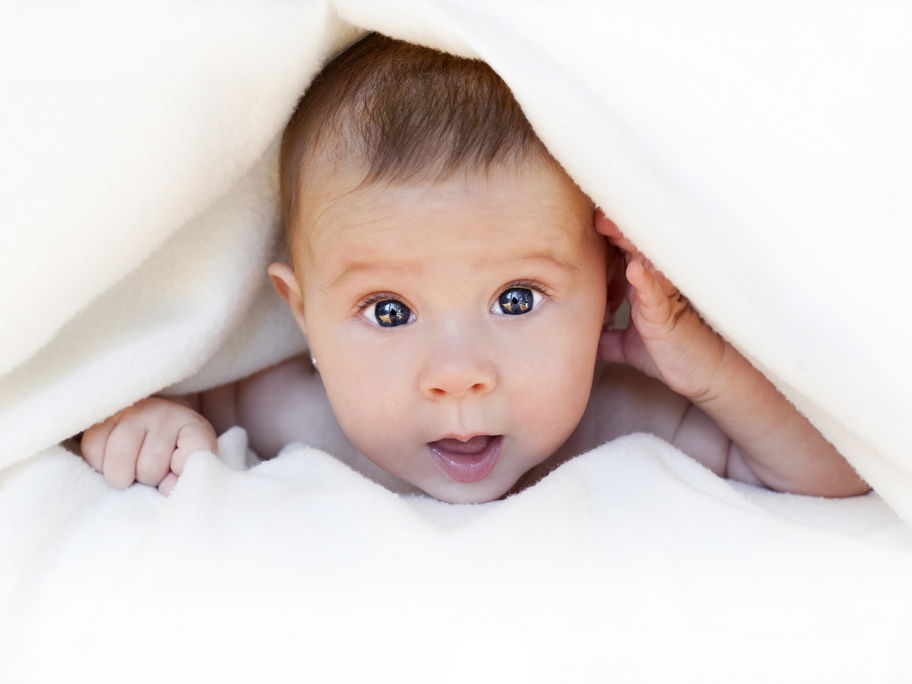 Baby guckt unter weißer Decke hervor.