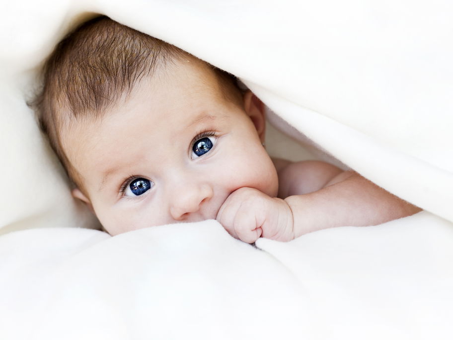 Baby guckt unter Decke hervor.