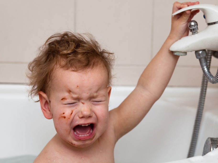 Ein Baby schreit beim Baden in der Badewanne und kneift dabei die Augen zu.