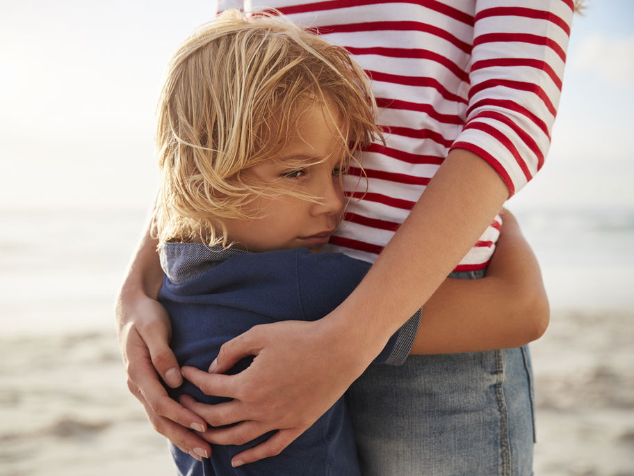 Mutter umarmt Sohn am Strand.
