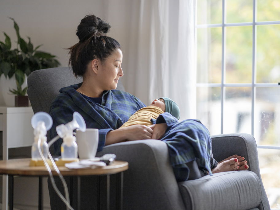 Eine Mama sitzt mit ihrem Baby und einer Milchpumpe auf dem Sofa.