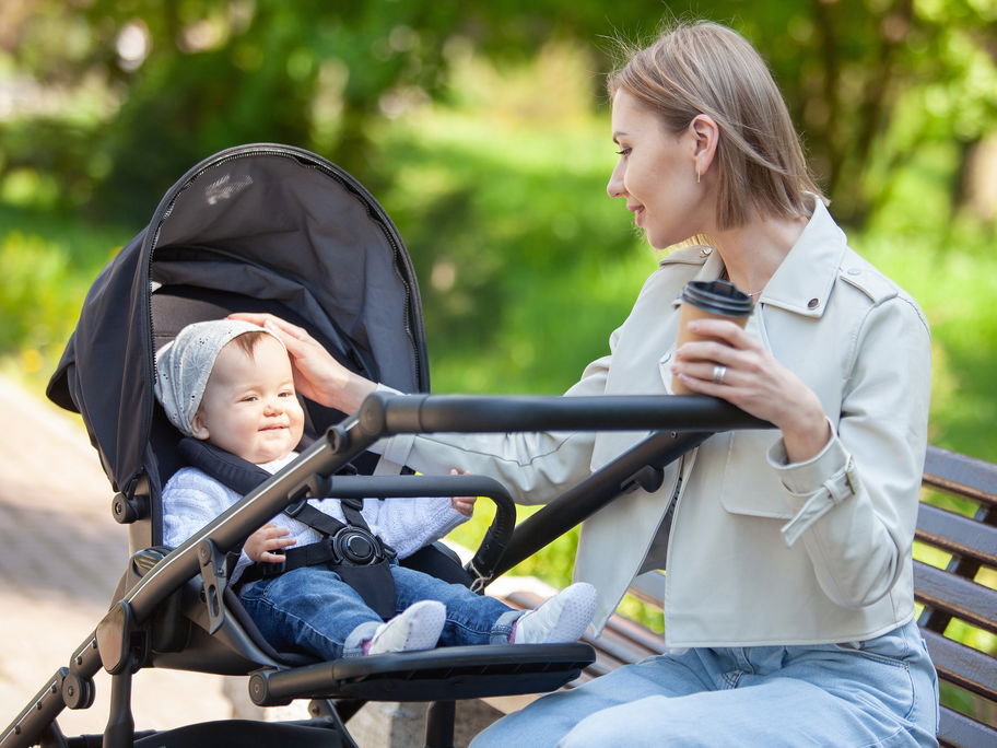 Eine Mutter streichelt ihr Baby im Kinderwagen über den Kopf.