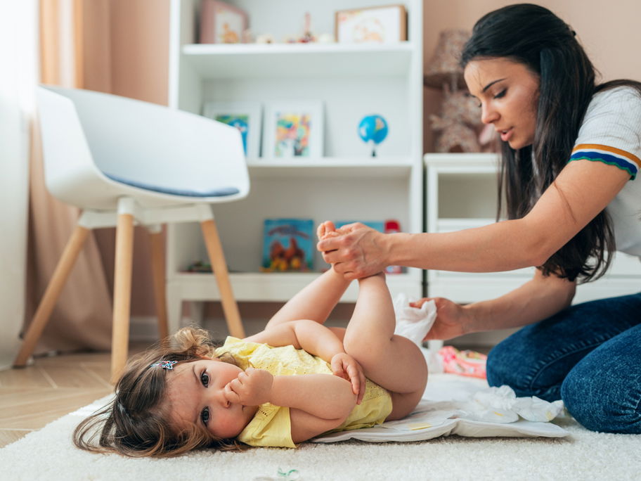 Junge Mutter wickelt ihr Baby auf dem Boden mit Feuchttüchern