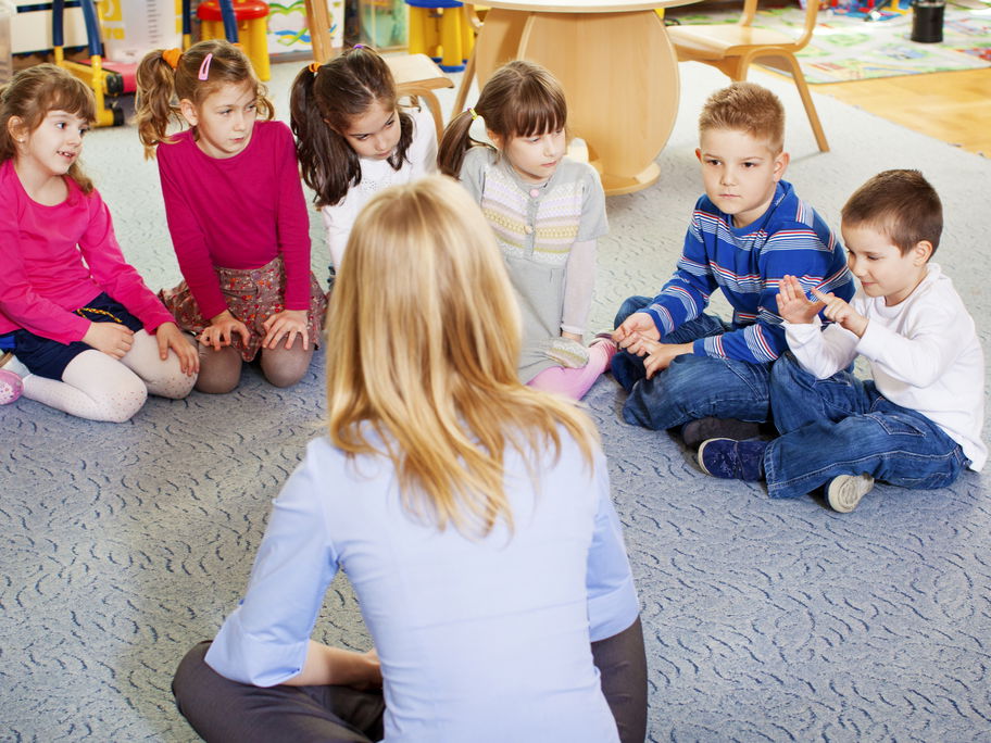 Kinder und Erzieherin sitzen im Kreis.