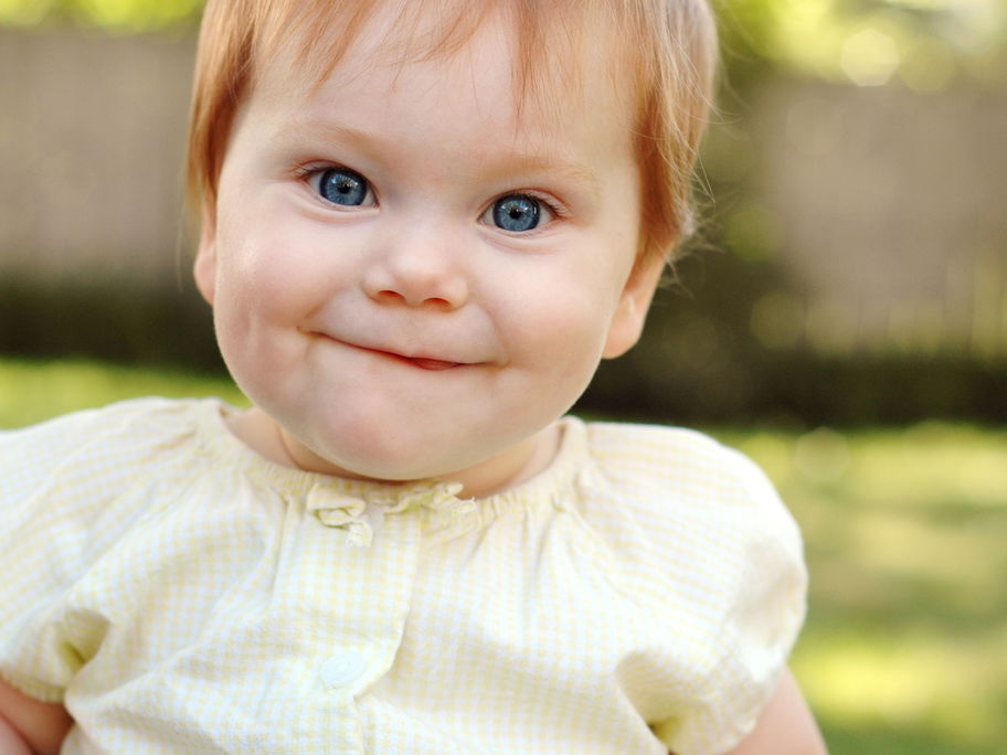 Ein Baby-Mädchen mit roten Haaren lächelt und freut sich über ihren englischen Mädchennamen.
