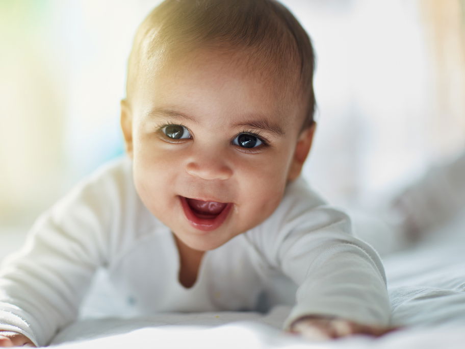 Ein Baby-Junge liegt auf dem Bett und ist fröhlich.