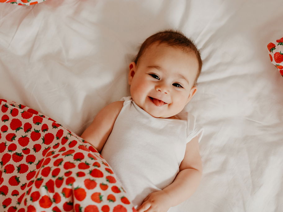 Kleines Baby-Mädchen lacht frech in die Kamera und liegt auf dem Boden.