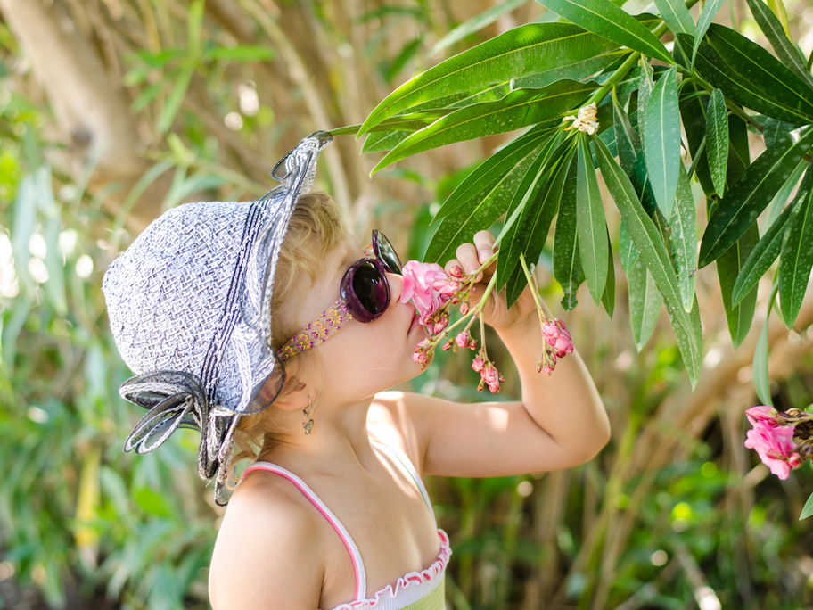 Mädchen mit Hut und Sonnenbrille riecht an einem Blumenstrauch im Garten