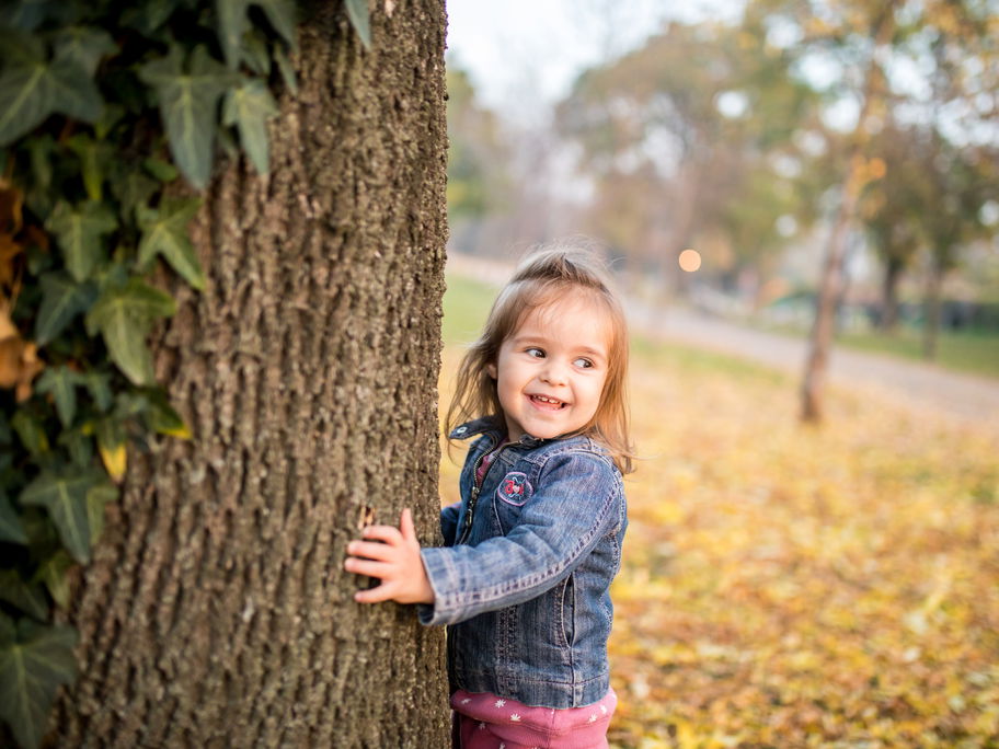 Fröhliches Kind läuft um Efeu-berankten Baum