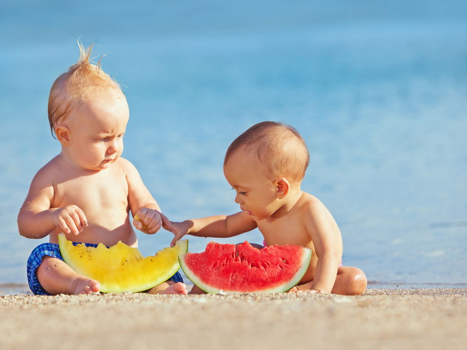 Zwei Babys essen am Strand Melone.