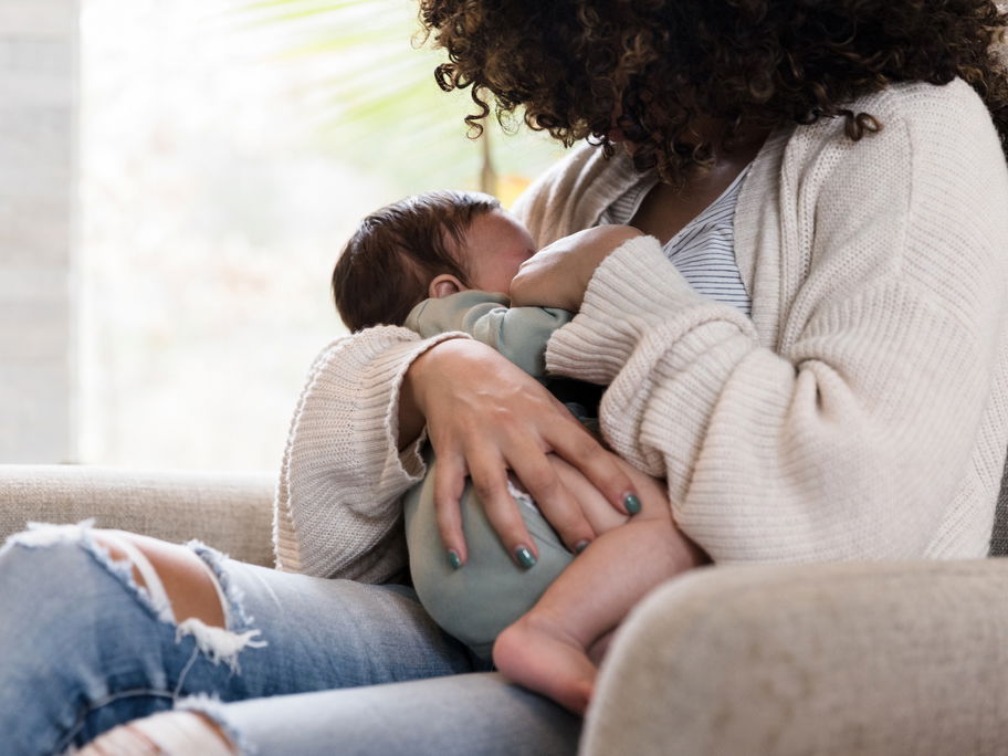 Eine Frau stillt ihr Baby sitzend auf dem Sessel.