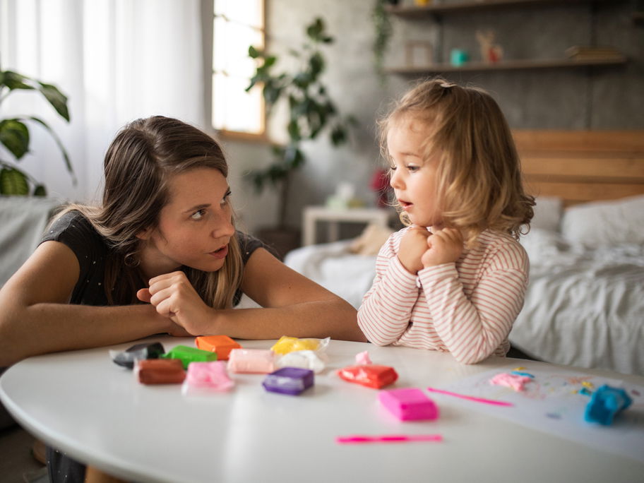 Mutter spricht mit ihrer kleinen Tochter am Spieltisch.