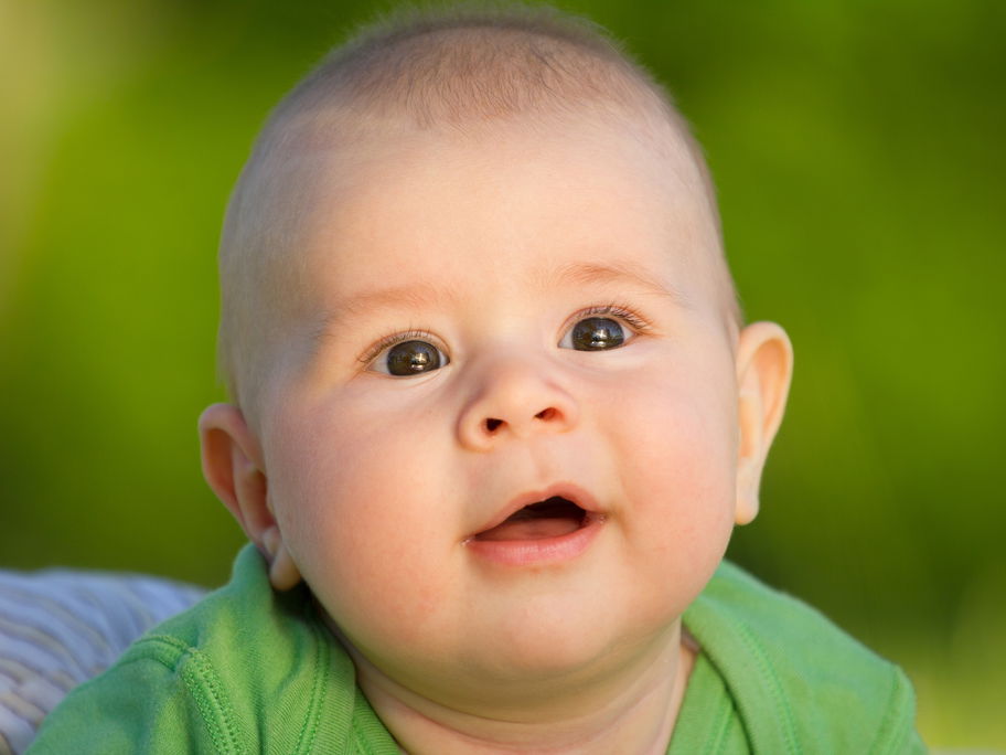 Baby-Junge grinst aufgeweckt nach vorne.