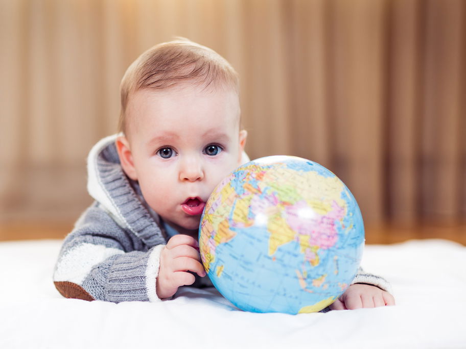Baby-Junge liegt auf dem Boden mit einem Globus in der Hand.
