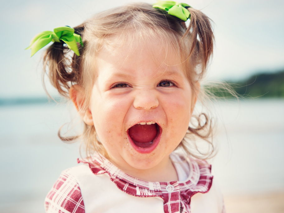 Kleines niedliches Baby-Mädchen lacht am Strand und freut sich über ihren starken Namen.