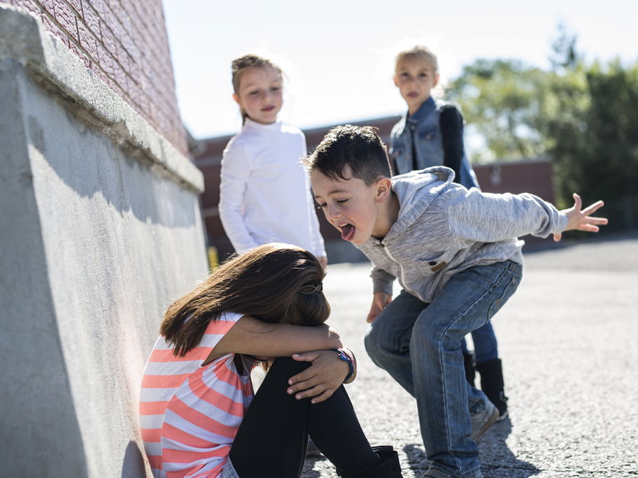 Mobbing an der Grundschule: Kinder ärgern ein kleines Mädchen auf dem Schulhof.