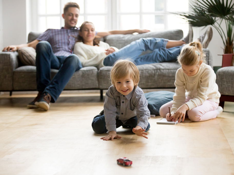Kinder spielen, Eltern sitzen entspannt auf dem Sofa.