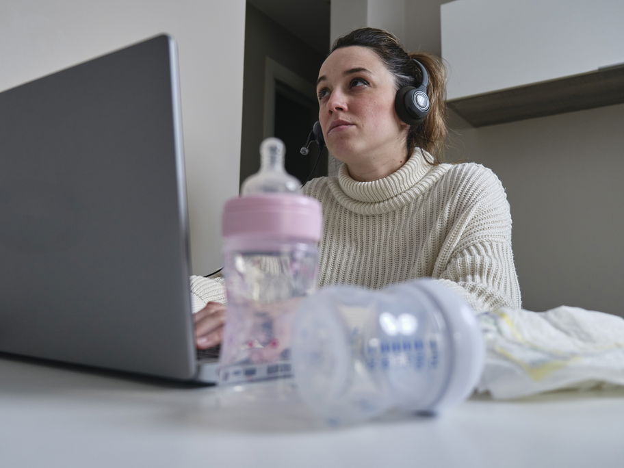 Mutter sitzt mit Milchflaschen und Windeln am Laptop.