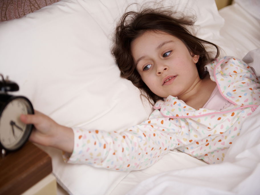 Mädchen liegt im Bett und stellt ihren Wecker aus.