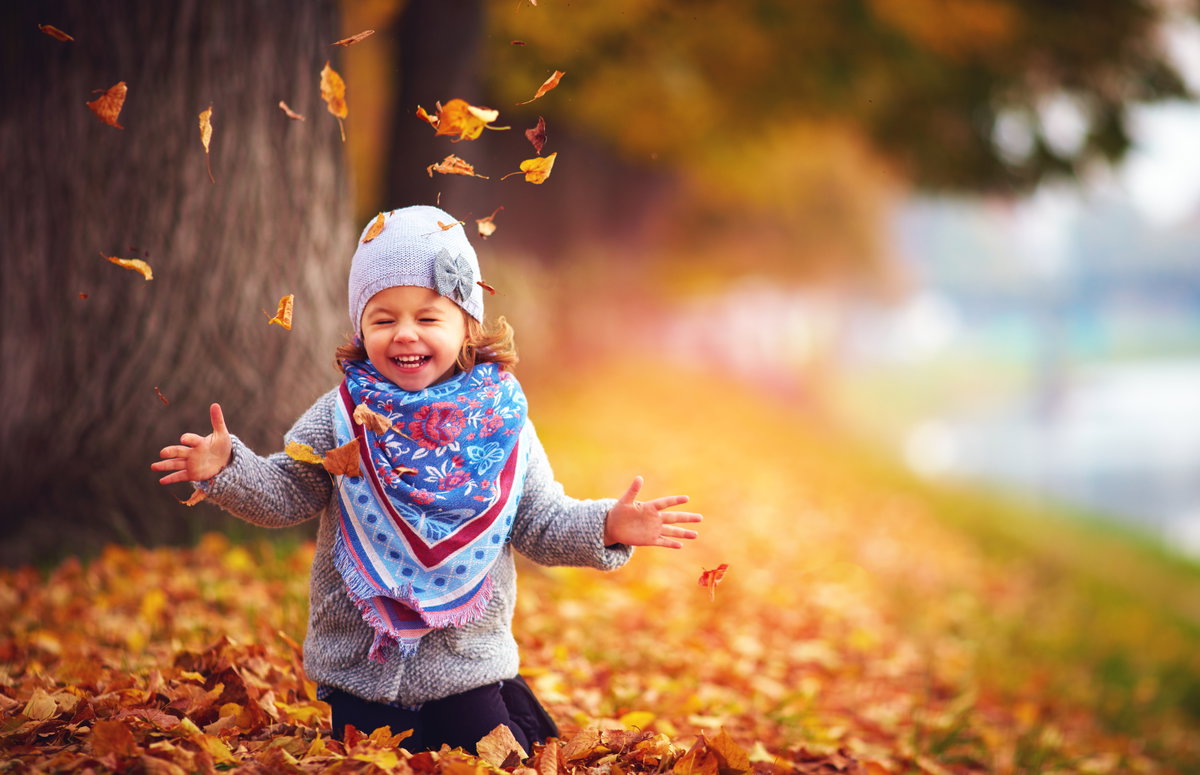 Ein Mädchen spielt im Herbstlaub.