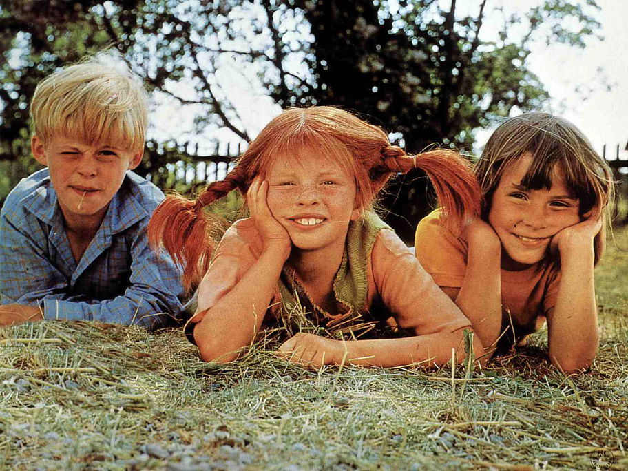Thomas, Pippi Langstrumpf und Annika liegen auf dem Rasen und schauen in die Kamera.