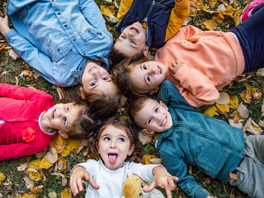 Kita-Kinder liegen im Herbstlaub und singen Herbstlieder im Kindergarten.